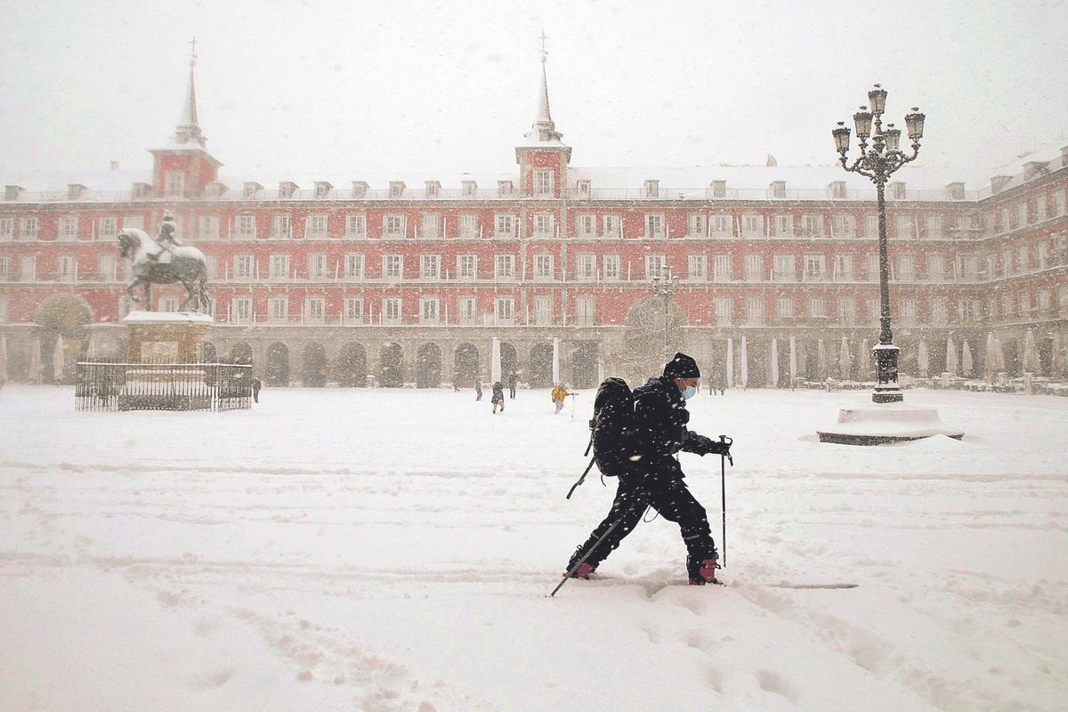 Un hombre pasea con sus esquís por la Plaza Mayor de Madrid durante la borrasca Filomena de 2021
