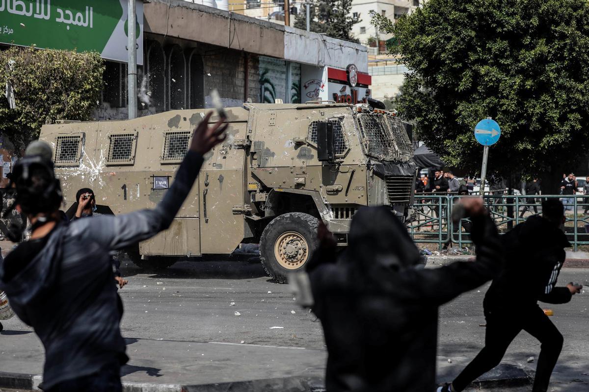 Un grupo de palestinos lanzan piedras contra un vehículo militar de Israel durante los enfrentamientos en la ciudad cisjordana de Nablús.