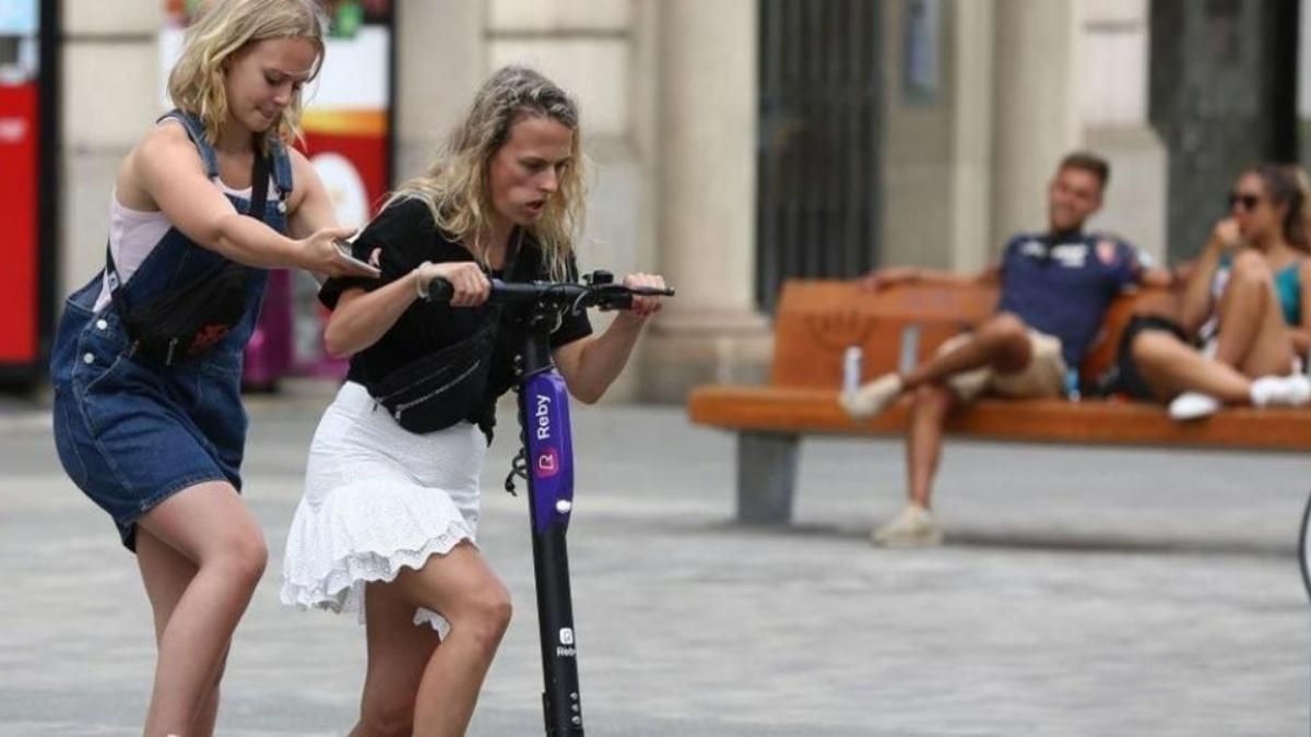 Dos jóvenes intentan subirse a un patinete compartido en Barcelona. Dos jóvenes intentan subirse a un patinete compartido en Barcelona.