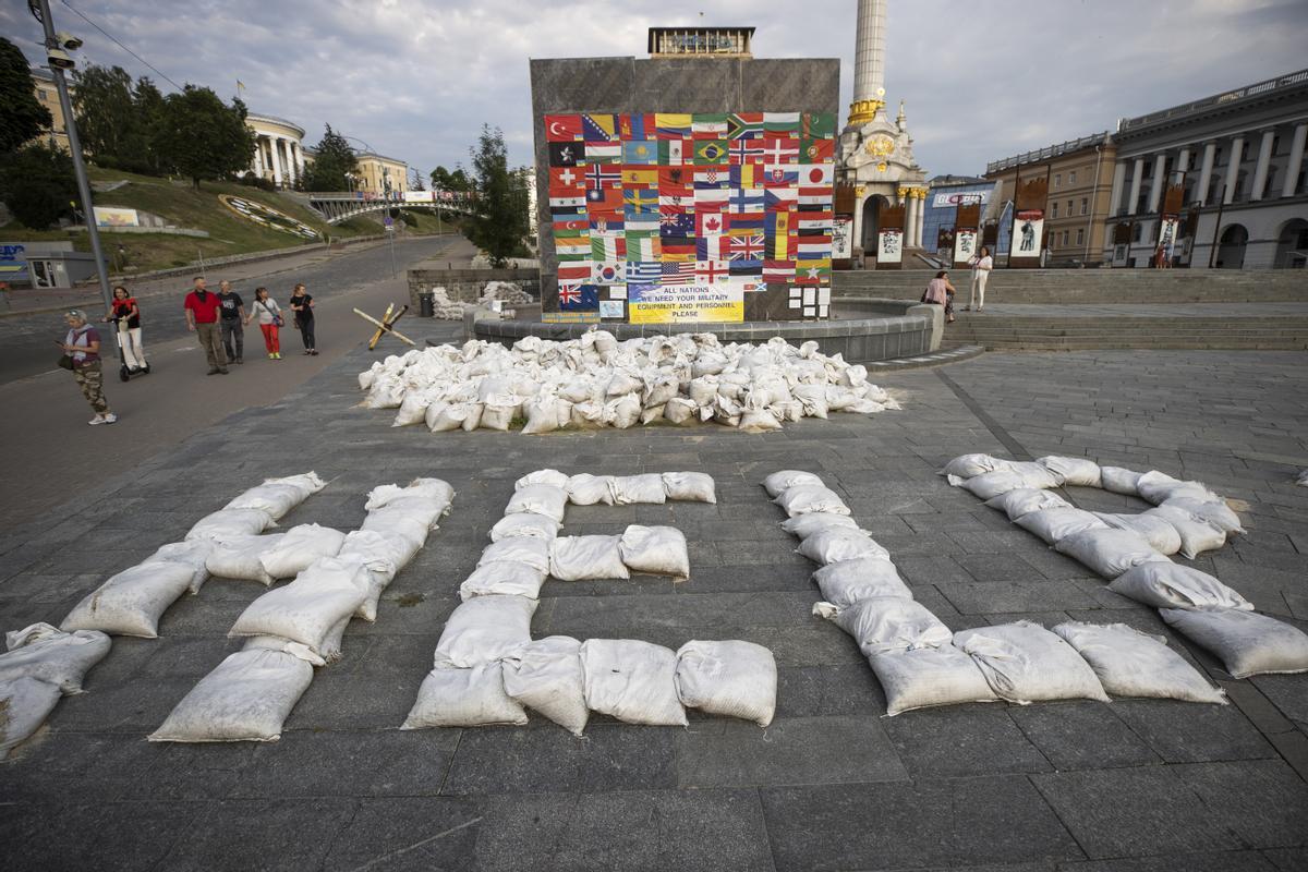 08/07/2022.- Personas caminan junto a un mensaje que pide ayuda al mundo, escrito con sacos de arenas, en la plaza Maidán, hoy, en Kiev (Ucrania).