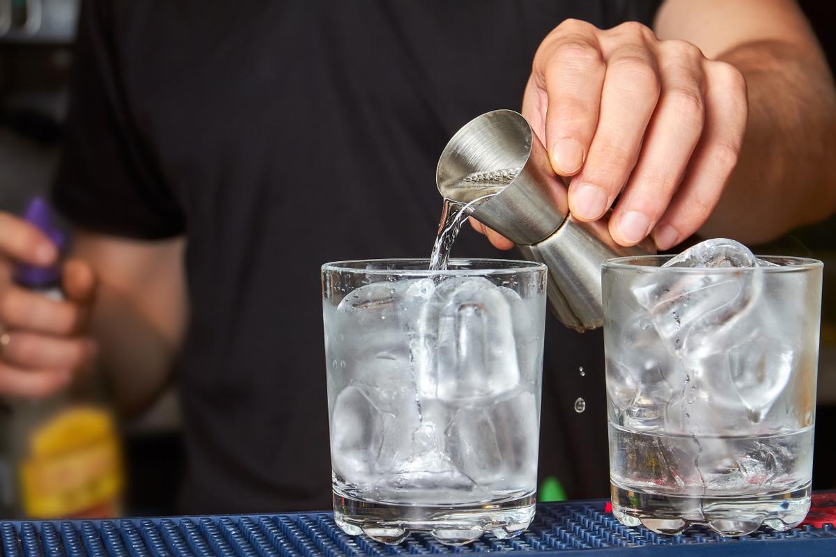 Camarero pone bebida en un vaso con hielo. 