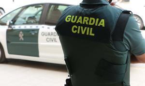 Archivo - Un agente de la Guardia Civil, de espaldas, junto a un vehículo oficial