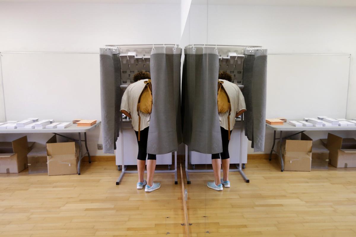 Un elector con su imagen reflejada en un espejo elige su papeleta para ejercer su derecho al voto en el Centro Cultural Volturno, en la localidad madrileña de Pozuelo de Alarcón.