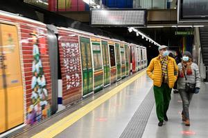 Dos personas caminan junto al tren de la línea 6 de metro de Madrid decorado con motivos navideños.