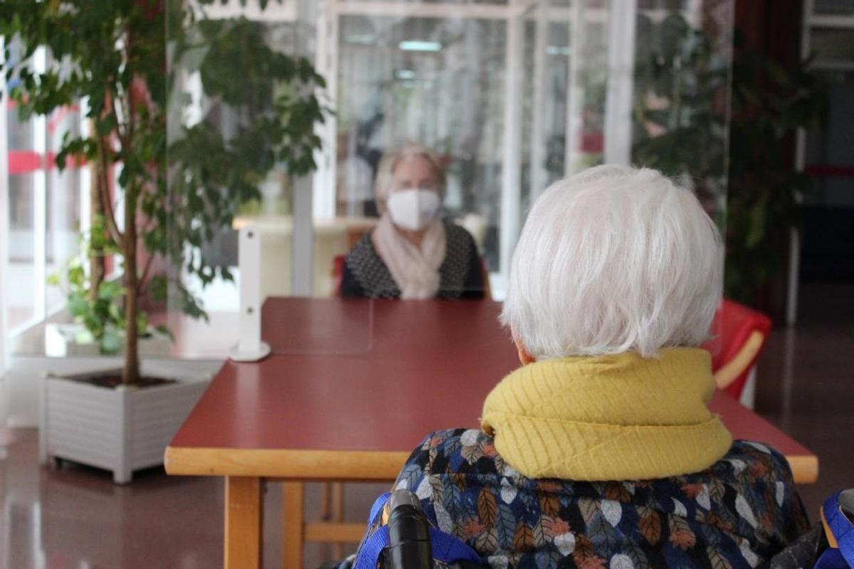 Dos personas con mascarilla y separadas por un panel de metacrilato en una residencia de mayores.