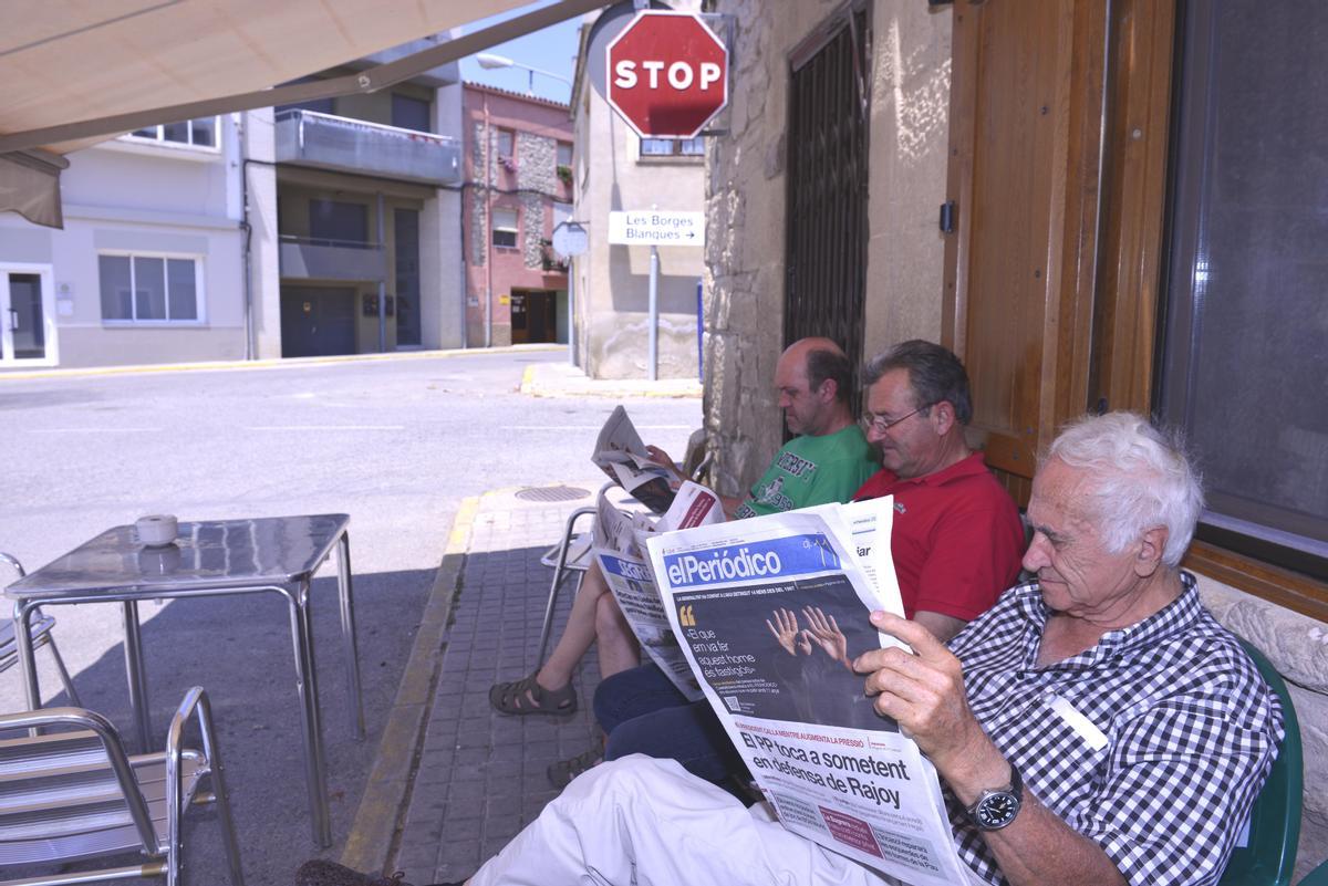 Tres señores leyendo El Periódico en un bar de pueblo.