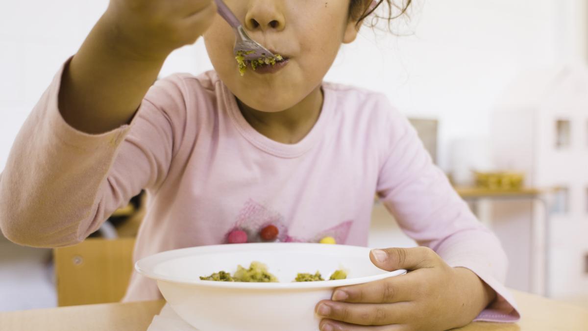 Una niña come en un comedor escolar. 
