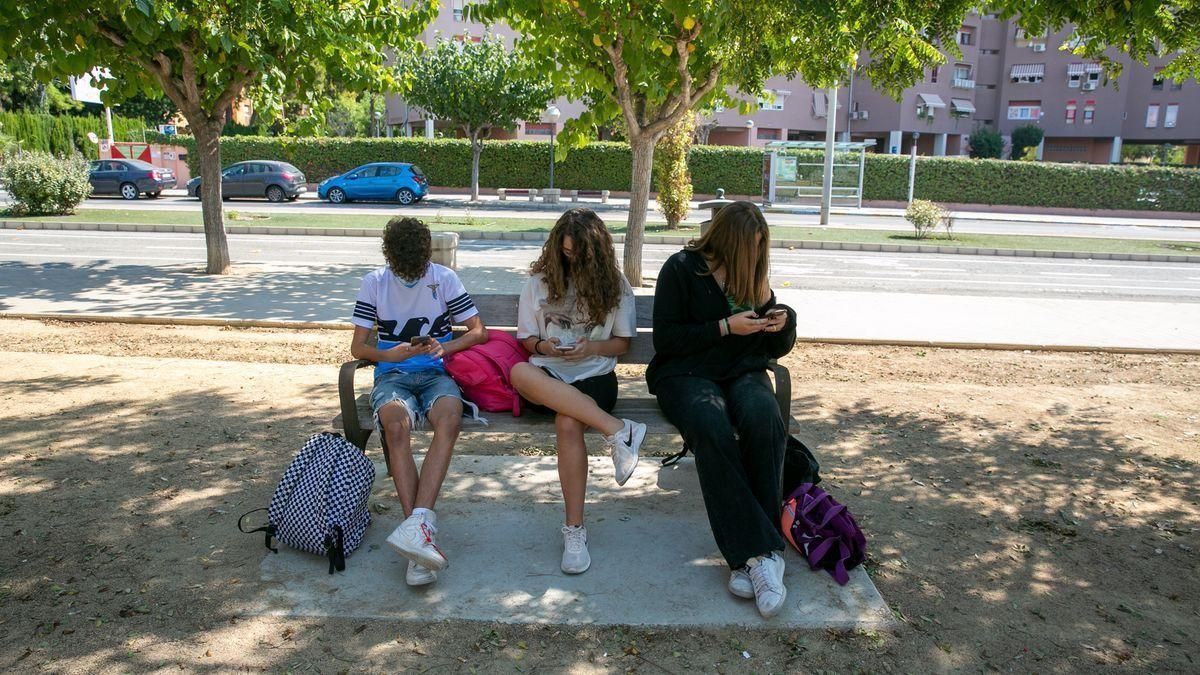 Tres jóvenes utilizan el móvil sentados en un banco. Tres jóvenes utilizan el móvil sentados en un banco.