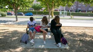 Tres jóvenes utilizan el móvil sentados en un banco.