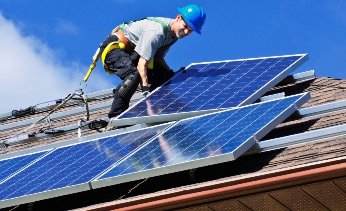 Un operario coloca varias placas solares en un tejado.