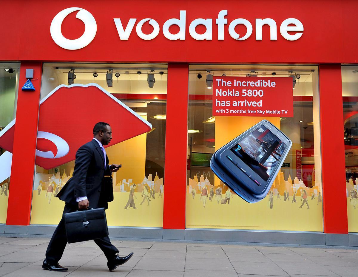 Una persona camina delante de una sede de Vodafone.