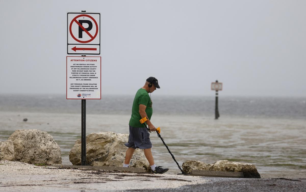 Un hombre camina con un detector de metales por lo que los lugareños reportaron como una costa expuesta por aguas mucho más retrocedidas de lo normal ante la llegada del huracán Ian, en Clearwater, Florida.