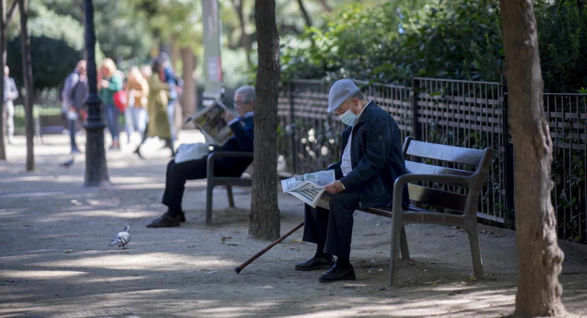 Personas mayores sentados en bancos en el parque de la Sagrada Familia, en Barcelona.