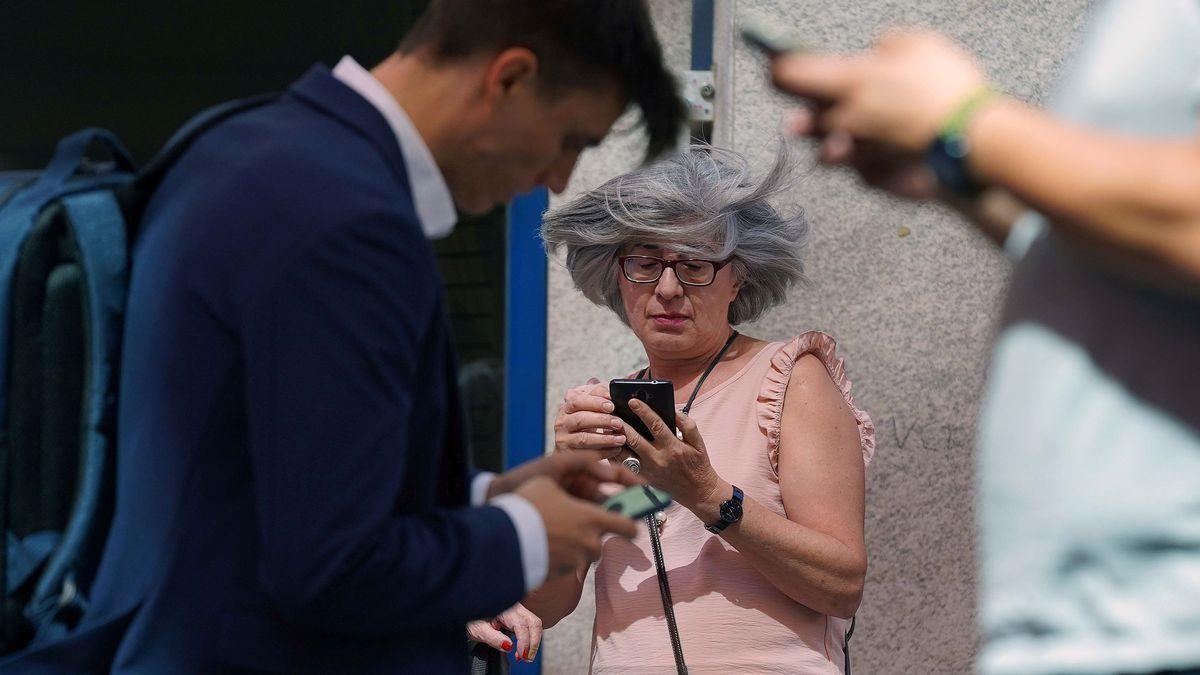 Tres personas miran sus teléfonos móviles en una calle de Madrid. Tres personas miran sus teléfonos móviles en una calle de Madrid.