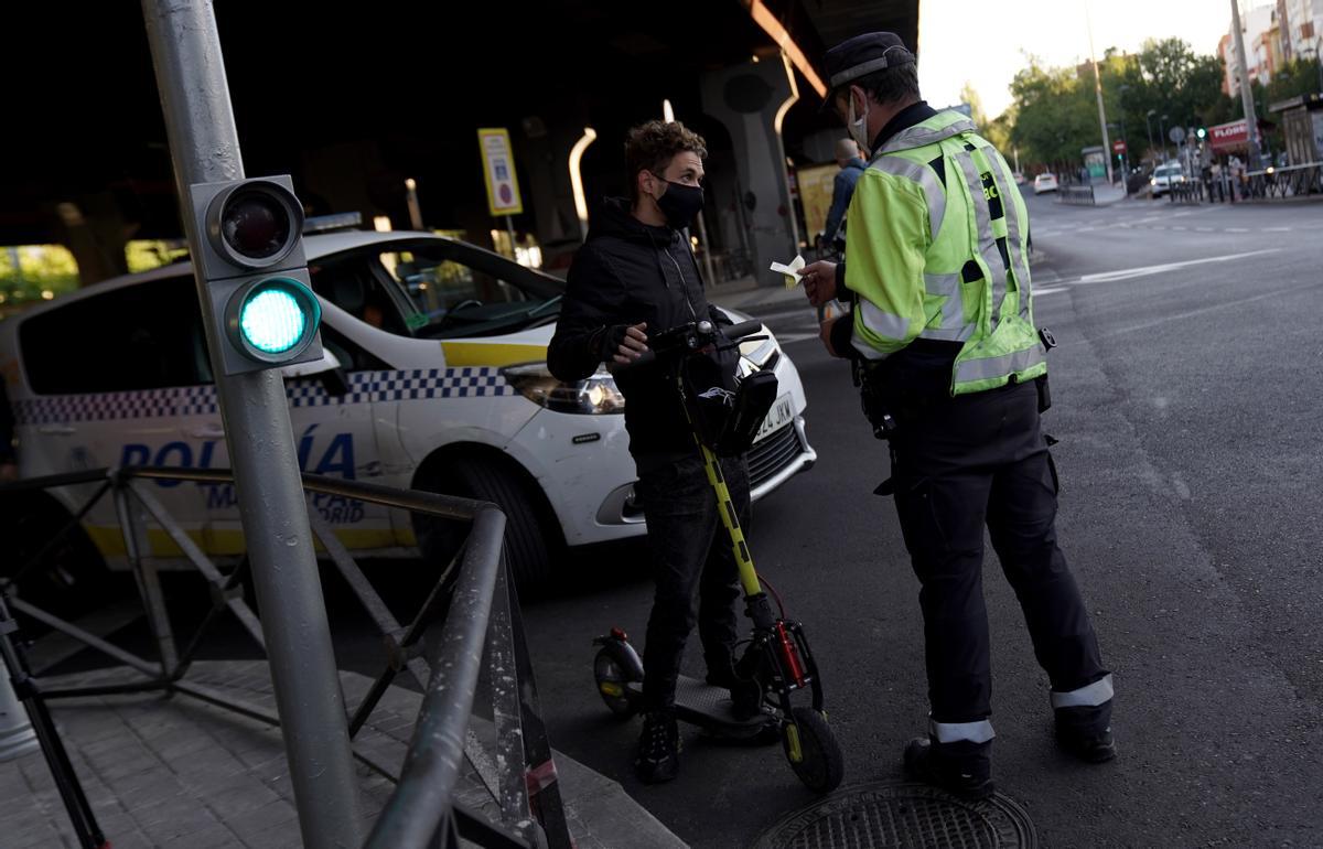Un policía municipal multa a una persona en patinete eléctrico por acceder a una zona confinada en Madrid en 2020.
