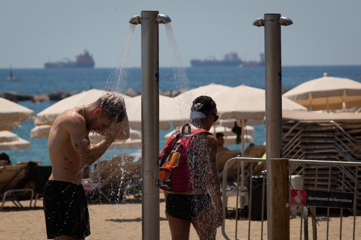 Varias personas se mojan en las duchas de la playa de la Barceloneta.