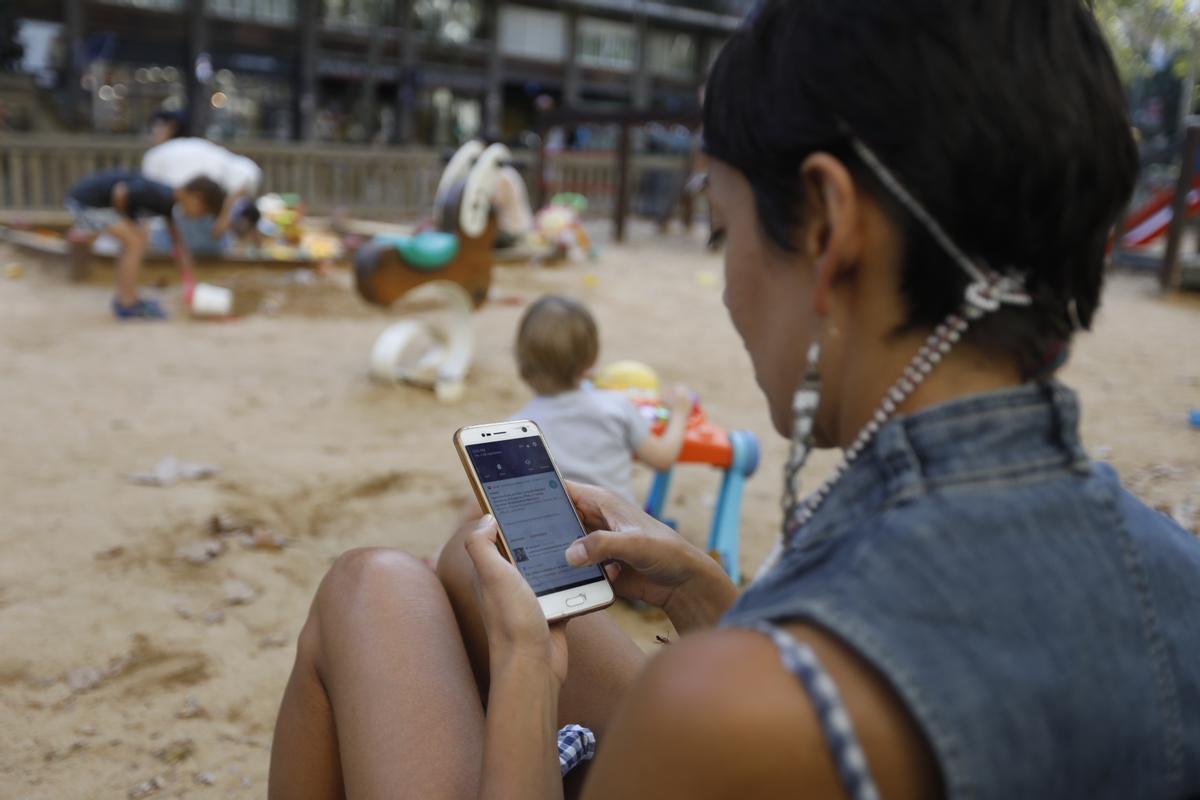 Una madre mira el móvil mientras los niños juegan. 