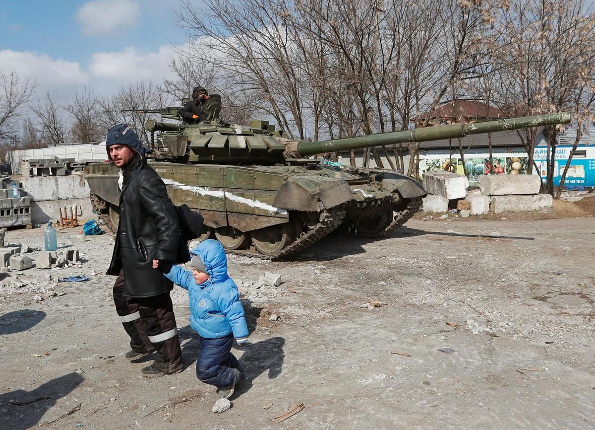 Un padre pasa junto a su hijo por delante de un tanque en Mariúpol.