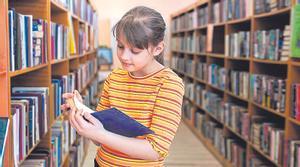 Una niña hojea un libro en una biblioteca