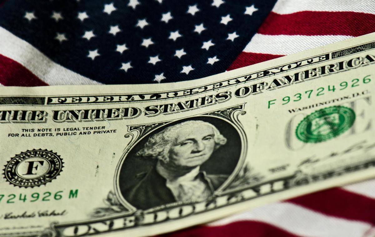 Un billete de un dólar por encima de una bandera de Estados Unidos. 