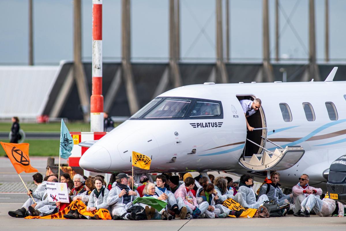 Activistas climáticos protestan bajo un avión privado en el Aeropuerto de Ámsterdam-Schiphol.