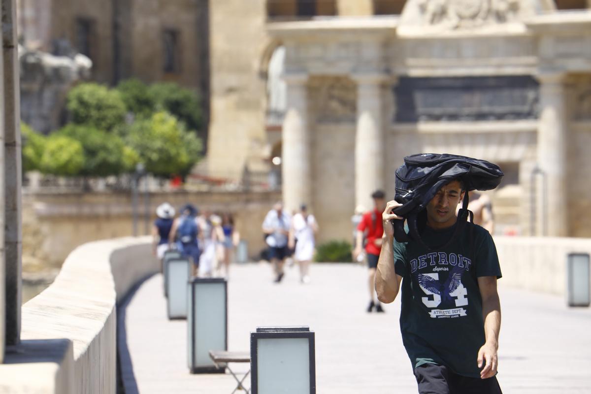 Un turista se protege del sol con una mochila mientras camina por Córdoba durante la ola de calor de mediados de junio.
