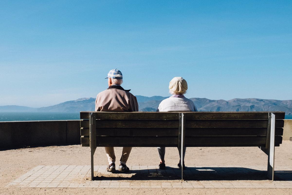 Dos personas sentadas en un banco frente al mar. 