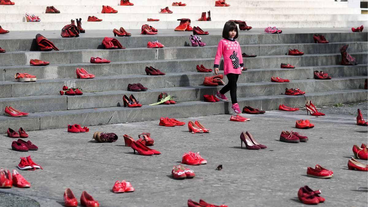 Una niña pasa por una instalación compuesta por zapatos rojos de mujer en una escalera.