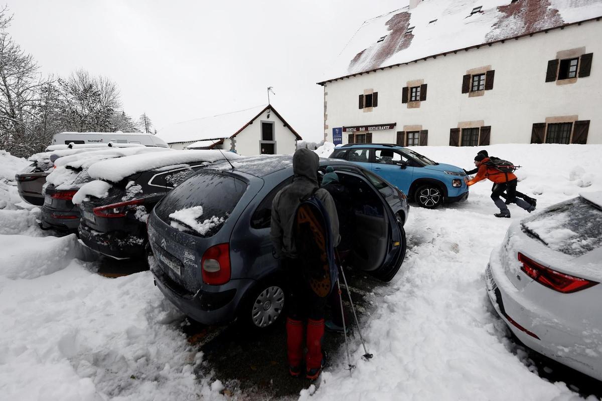Dos personas empujan un vehículo que ha quedado atrapado en la nieve en el parking de Roncesvalles este domingo. EFE/ Jesús Diges
