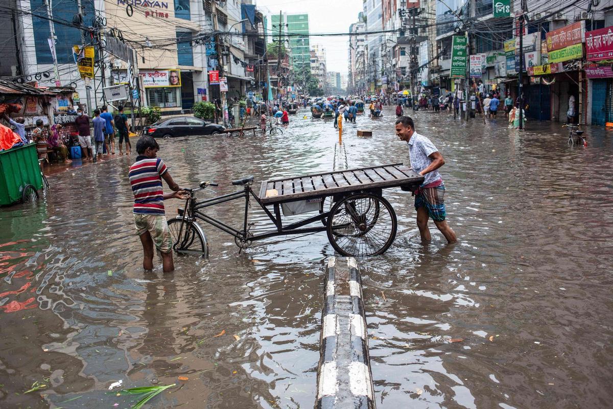 Dos hombres intentan mover su bicicleta de tres ruedas a través de la inundada Green Road en Dhaka tras las fuertes lluvias.