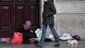 Una transeúnte pasa por delante de una mujer sin hogar.