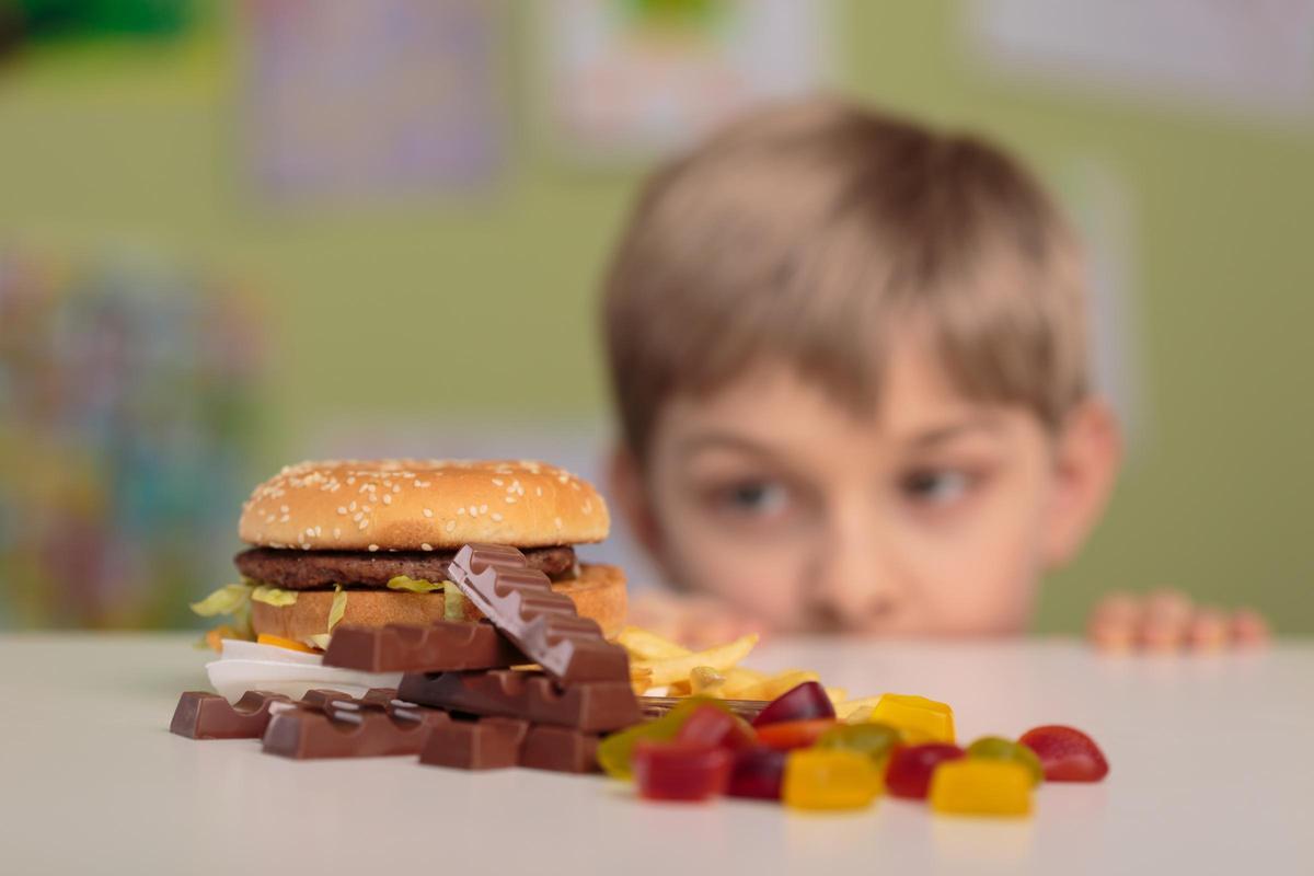 Un niño observa una mesa con comida basura. Un niño observa una mesa con comida basura.