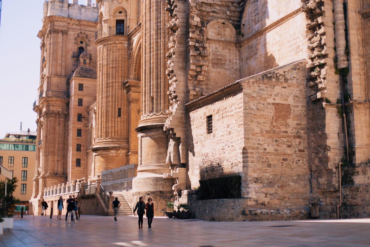 Dos personas caminan delante de la catedral de Málaga. 
