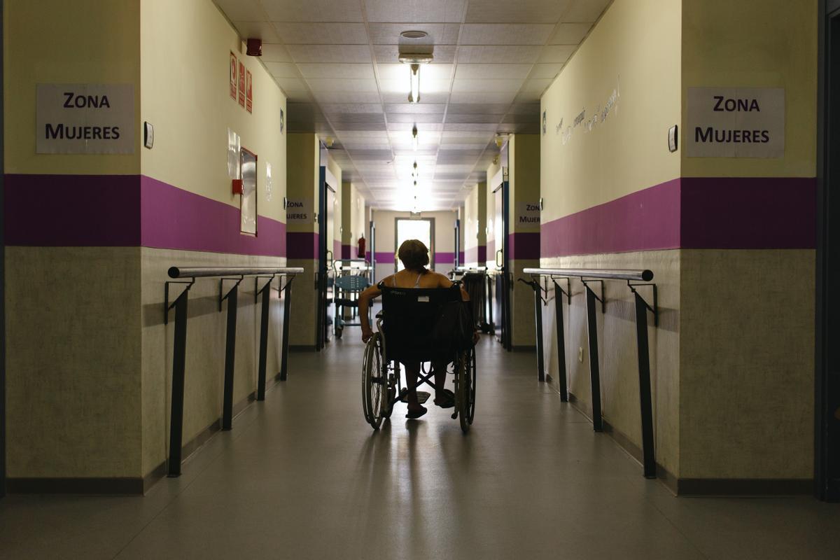 Una residente recorre en silla de ruedas el pasillo de las habitaciones del Centro de acogida a personas sin hogar de Puerta Abierta.